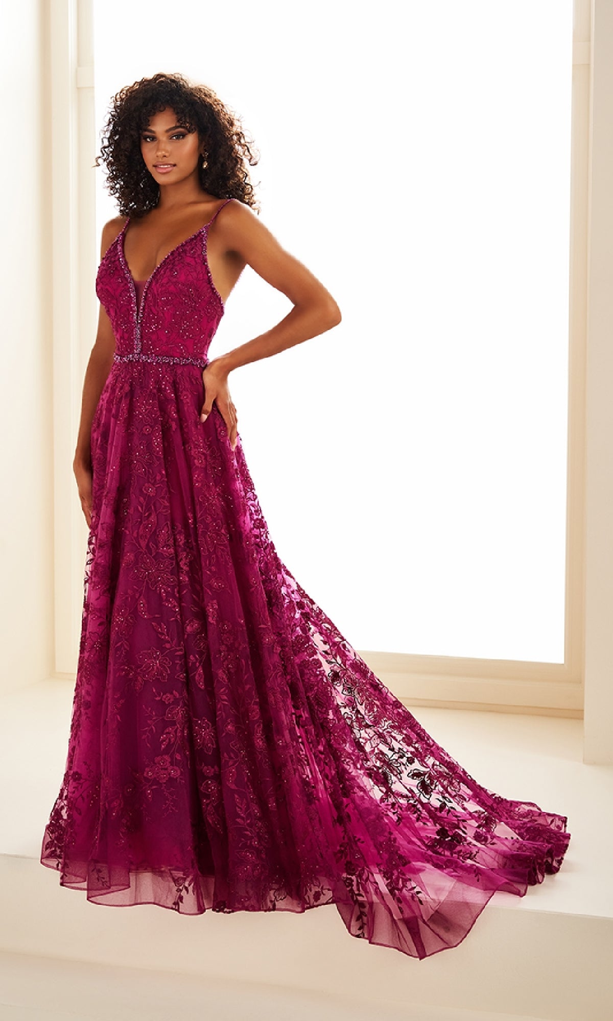 A woman in the Ellie Wilde EW36088 long prom dress with an embroidered tulle bodice, beaded waist, A-line skirt, and pockets stands in a well-lit room.